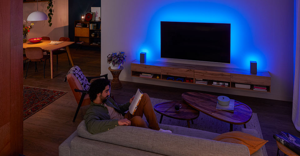 Muž si už&iacute;v&aacute; televizor Philips Ambilight připojen&yacute; k wi-fi reproduktorům Philips TAW6205