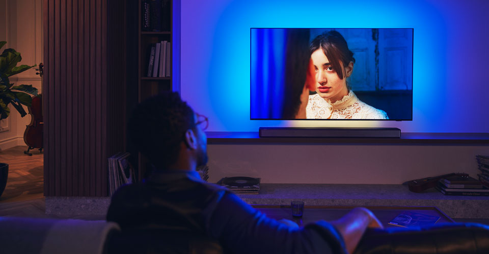 Muž si už&iacute;v&aacute; Philips Ambilight TV se soundbarem