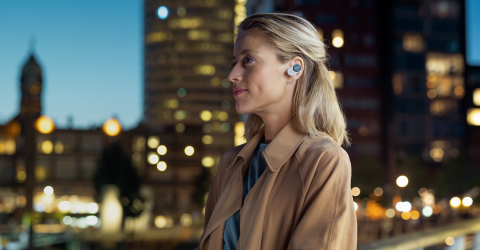 Žena nos&iacute; sluch&aacute;tka do u&scaron;&iacute; Philips s potlačen&iacute;m hluku venku ve městě