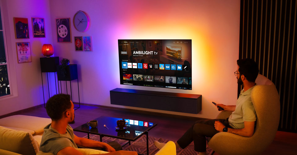 Dva muži sleduj&iacute; n&aacute;stěnn&yacute; televizor Ambilight v ob&yacute;vac&iacute;m pokoji